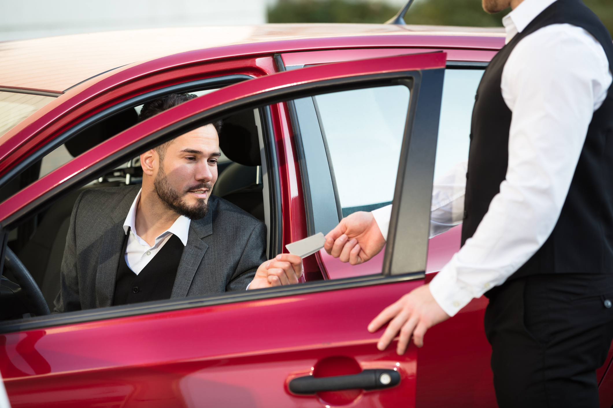 Valet Giving Receipt To Young Male Businessperson Sitting Inside Red Car